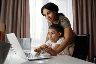 Mother helps her daughter use a laptop